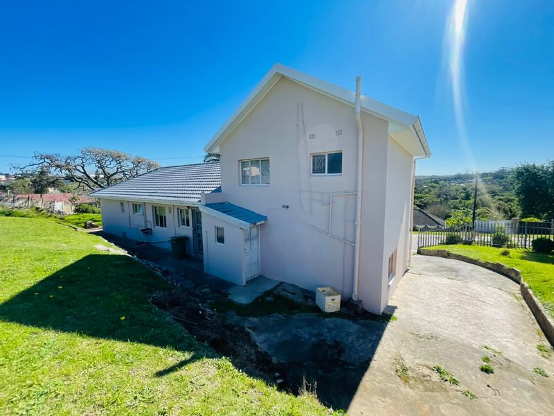 Rear view of the property showing the building facade, tiled roof, concrete driveway, and surrounding garden area.
