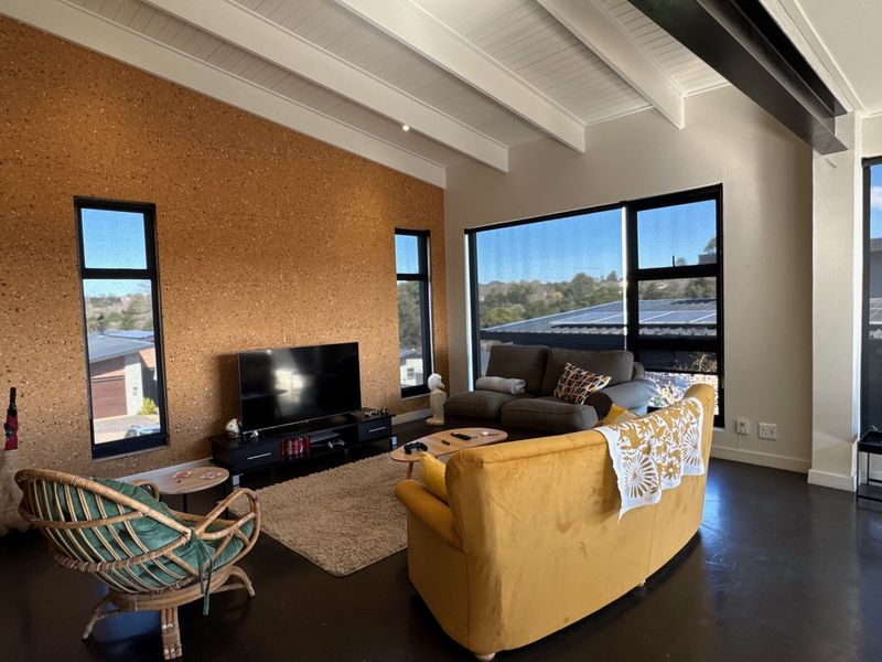 Spacious living room featuring a unique cork accent wall, exposed beam vaulted ceiling, polished concrete floors, and large windows with scenic views.