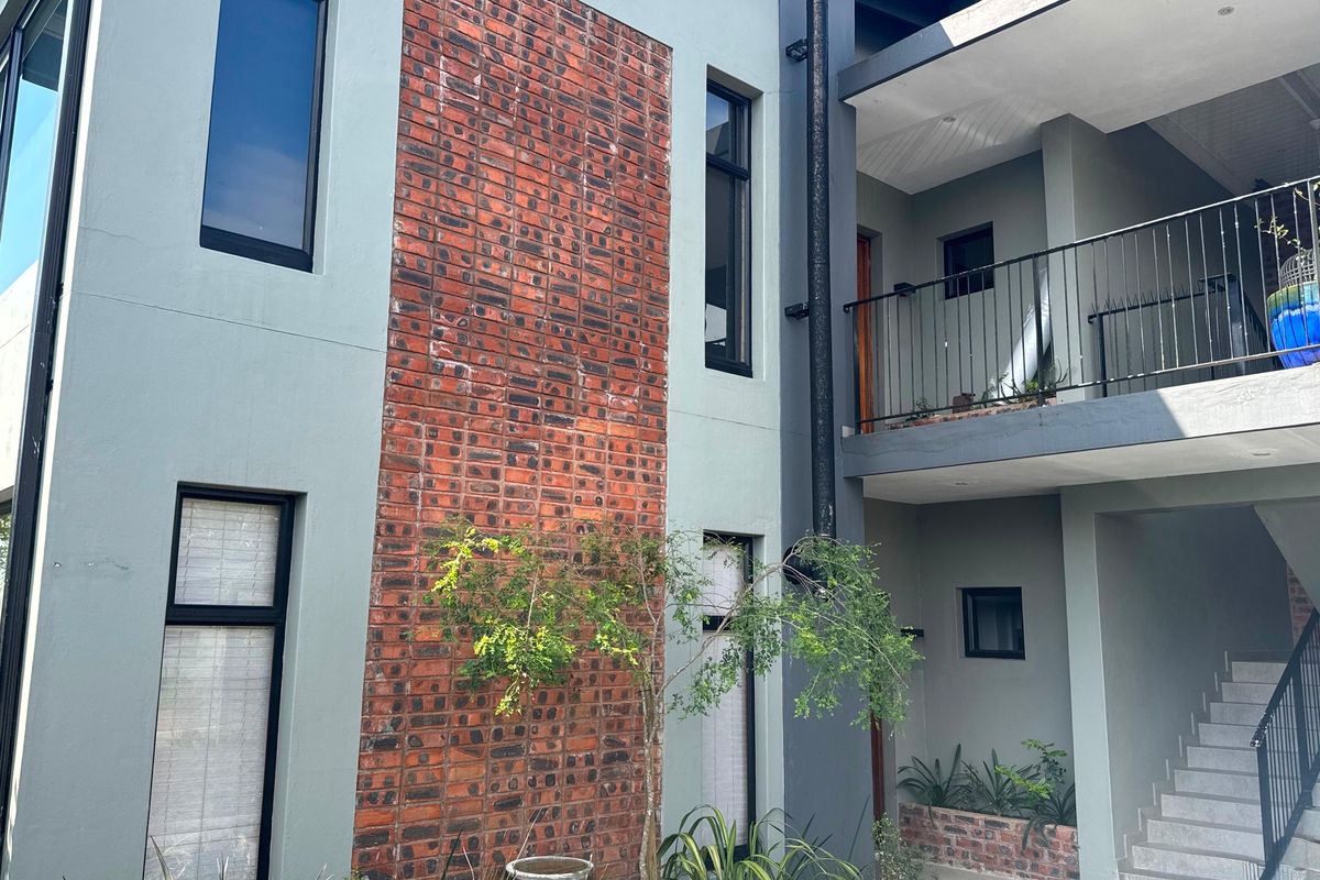 A modern apartment exterior featuring a combination of painted render and exposed brickwork, with a concrete staircase and balcony access.