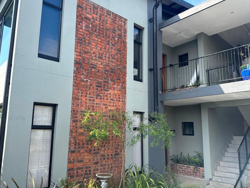 A modern apartment exterior featuring a combination of painted render and exposed brickwork, with a concrete staircase and balcony access.