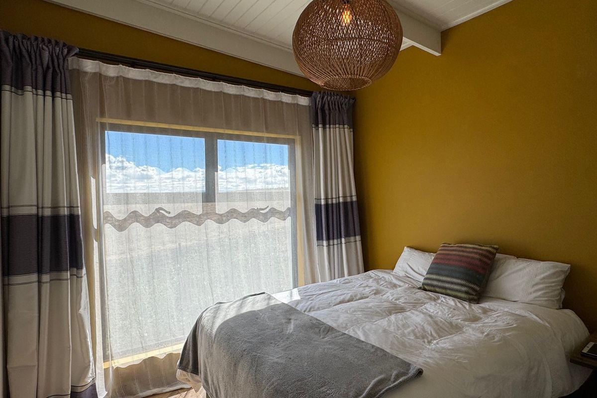 A cozy bedroom featuring a high exposed beam ceiling, warm yellow walls, and a large window allowing for natural light.