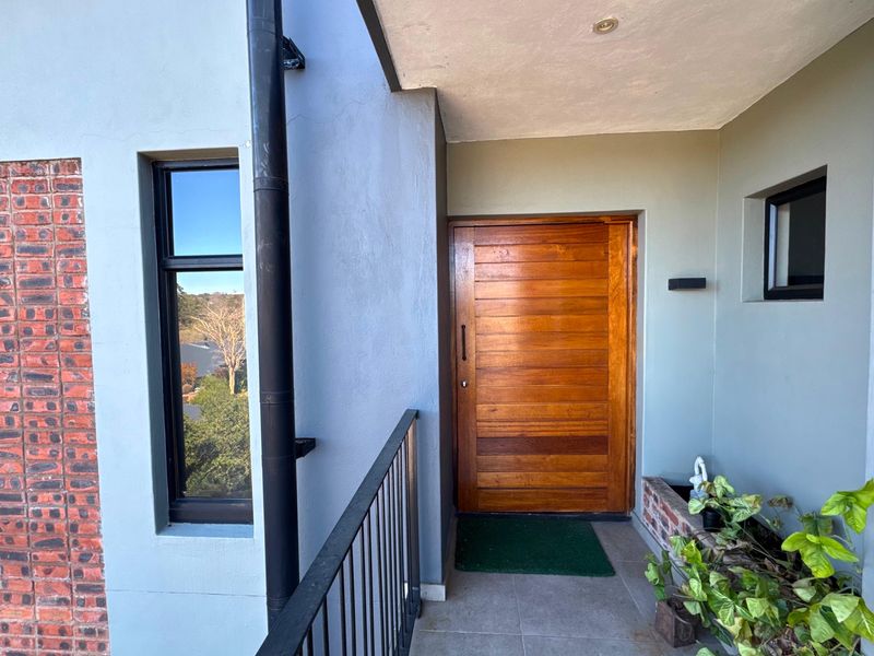 A modern apartment entrance featuring a solid timber front door, black metal balustrade, and a decorative brick feature wall.