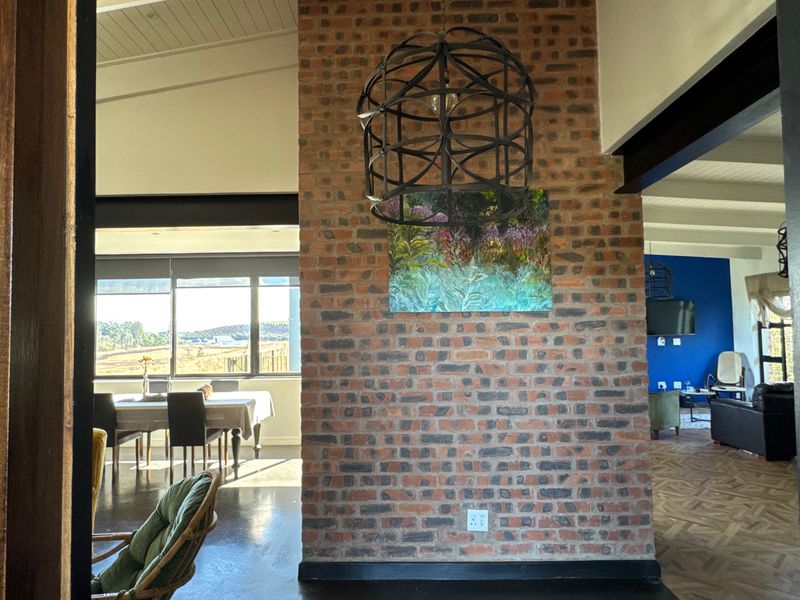 Spacious open-plan living area featuring a prominent exposed brick wall, high ceilings with exposed beams, and large windows providing natural light and scenic views.