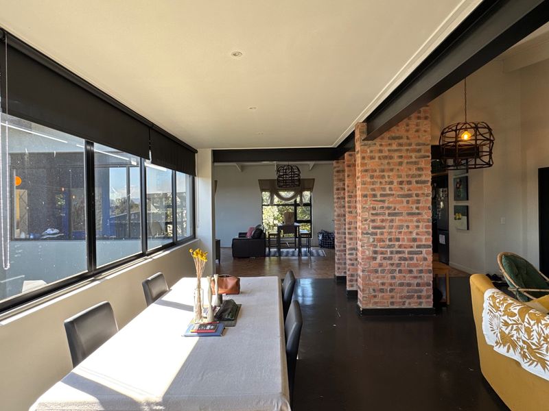 Spacious open-plan living and dining area featuring industrial-style exposed brick columns, steel beams, polished concrete floors, and large windows providing ample natural light.