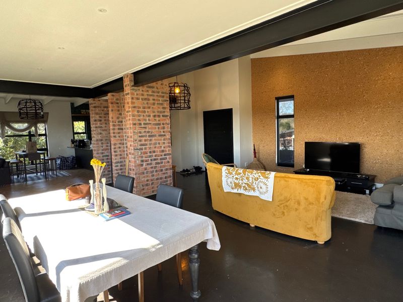 Spacious open-plan living and dining area featuring exposed brick columns, industrial steel beams, a unique cork feature wall, and polished concrete floors.
