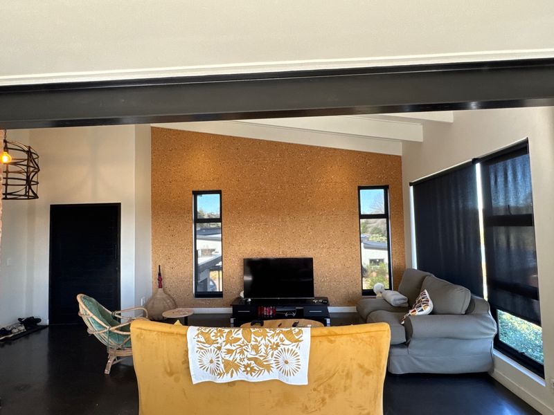 A modern living room featuring a distinctive cork feature wall, exposed ceiling beams, and large vertical windows that provide ample natural light.