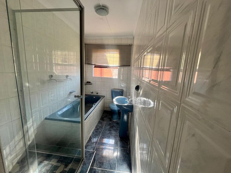 A dated bathroom featuring a blue pedestal sink, matching toilet, built-in bathtub, and a separate glass-enclosed shower area with white wall tiling.