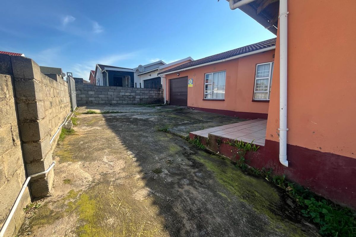 Rear exterior view showing a concrete driveway, boundary wall, and access to the garage with visible wear on the paving and exterior finishes.