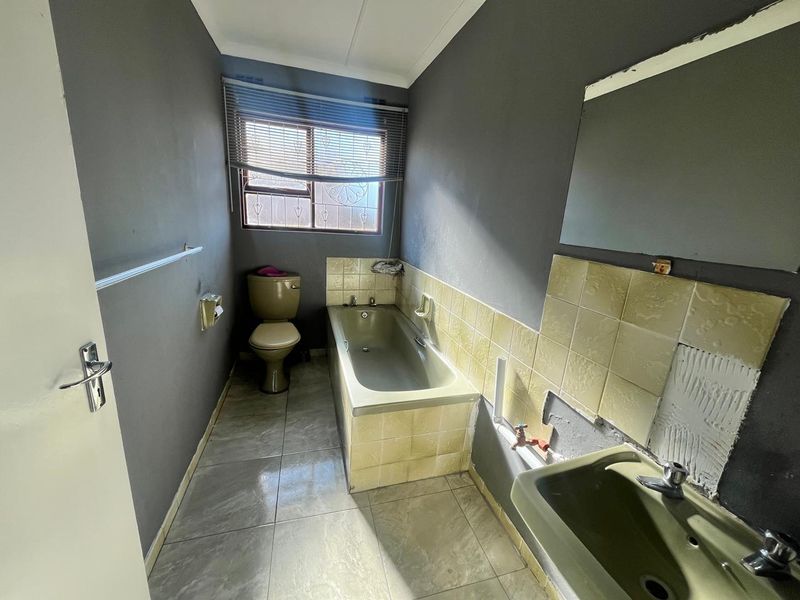 A dated bathroom featuring a bathtub, toilet, and pedestal basin, currently requiring renovation and tile repairs to modernize the space.