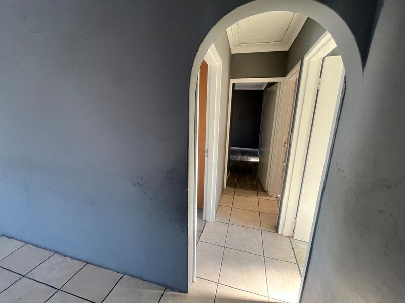 A vacant hallway featuring arched architectural detailing, tiled flooring, and multiple doorways leading to adjacent rooms, showing signs of wear on the wall surfaces.