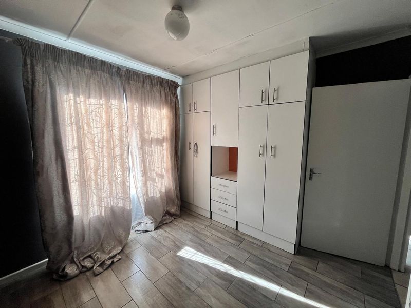 A bedroom featuring built-in white cupboards, wood-look tiled flooring, and natural light through the window.
