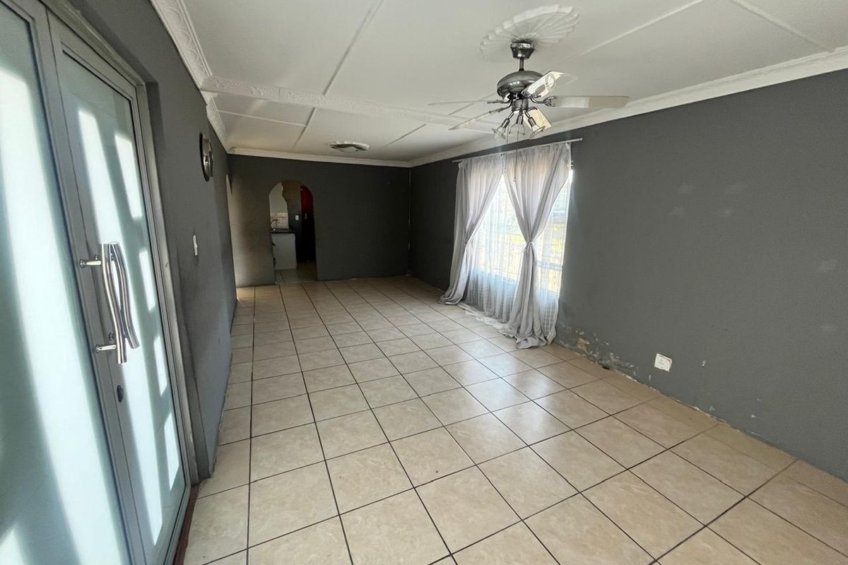An empty living room featuring tiled flooring, a ceiling fan, and an archway leading to an adjacent space, with visible wall finish deterioration.