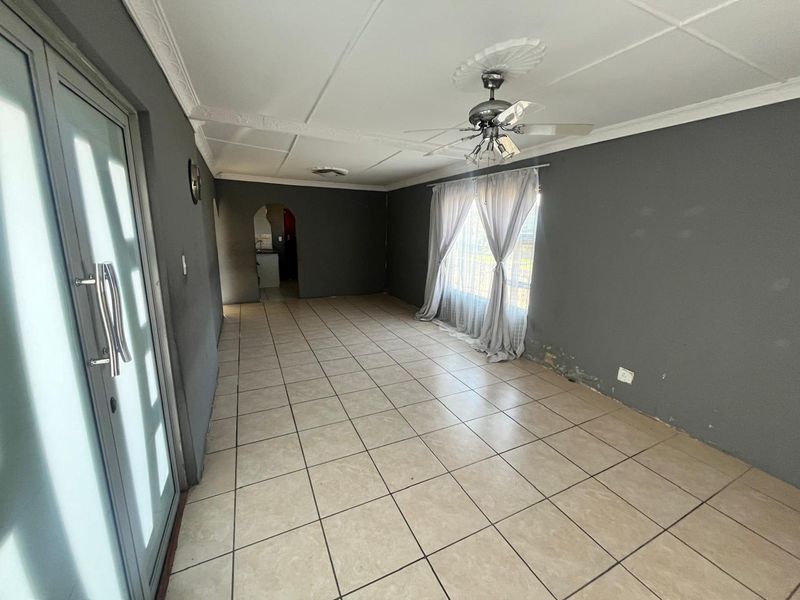 An empty living room featuring tiled flooring, a ceiling fan, and an archway leading to an adjacent space, with visible wall finish deterioration.