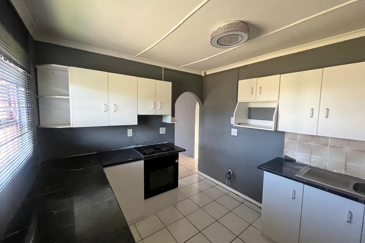 A functional kitchen featuring white cabinetry, dark countertops, built-in oven and hob, and tiled flooring, providing a clean and practical workspace.