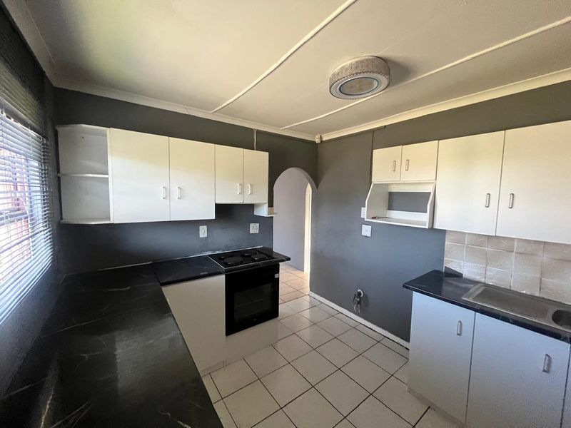 A functional kitchen featuring white cabinetry, dark countertops, built-in oven and hob, and tiled flooring, providing a clean and practical workspace.