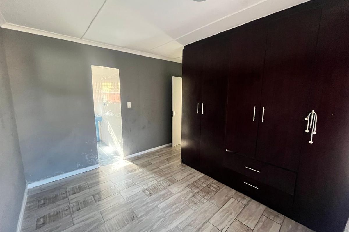 A vacant bedroom featuring dark built-in cupboards, wood-look tiled flooring, and neutral grey walls, offering a clean canvas for personalization.