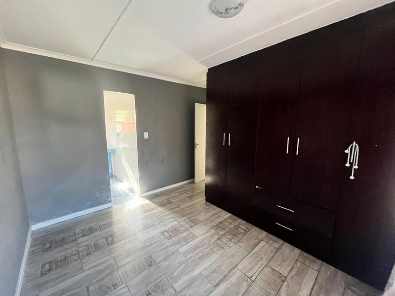 A vacant bedroom featuring dark built-in cupboards, wood-look tiled flooring, and neutral grey walls, offering a clean canvas for personalization.