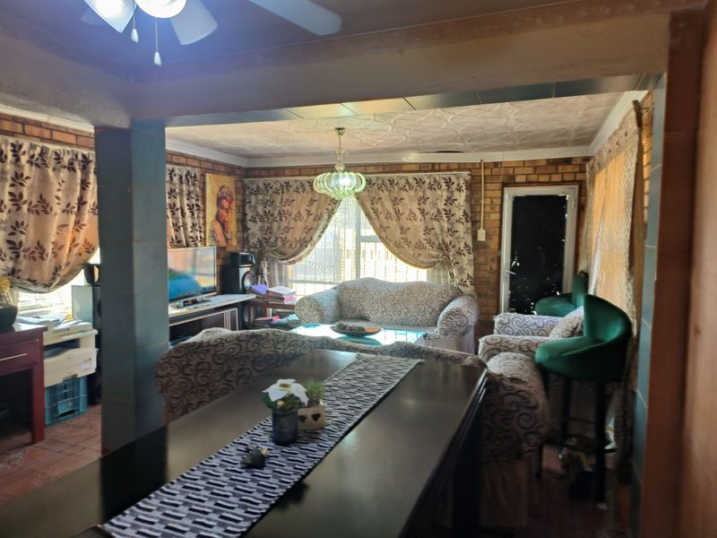 Open plan living area featuring exposed brick walls, decorative ceiling tiles, and a ceiling fan, offering a rustic aesthetic with potential for modernization.