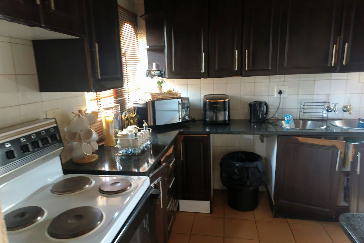 A functional kitchen featuring dark wood cabinetry, granite countertops, a tiled backsplash, and an electric stove with tiled flooring.