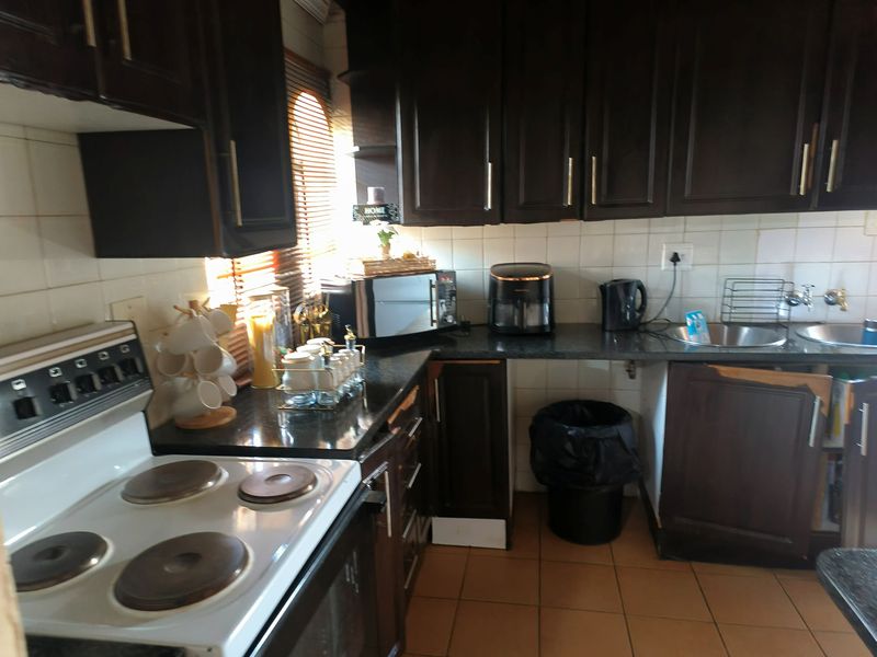 A functional kitchen featuring dark wood cabinetry, granite countertops, a tiled backsplash, and an electric stove with tiled flooring.