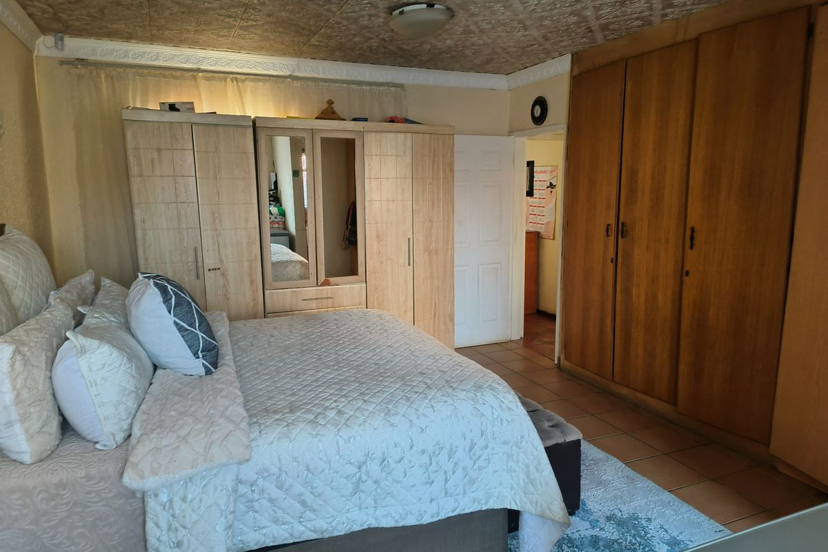 A bedroom featuring built-in wooden cupboards, tiled flooring, and a textured ceiling, offering a functional space with potential for modern updates.