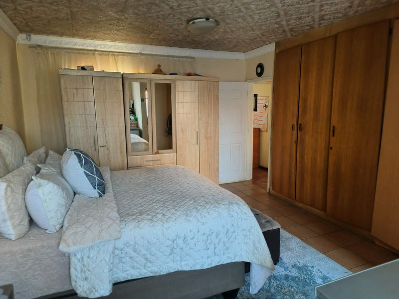 A bedroom featuring built-in wooden cupboards, tiled flooring, and a textured ceiling, offering a functional space with potential for modern updates.