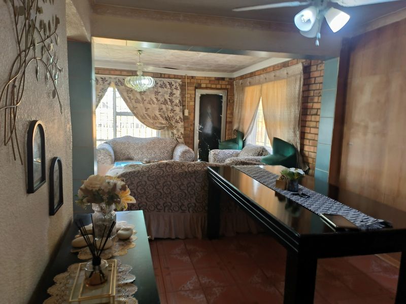 A living area featuring exposed brick walls, tiled flooring, and a ceiling fan, offering a dated aesthetic with potential for modernization.