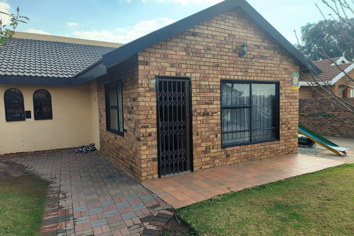 Rear view of the house featuring a face brick facade, tiled patio area, paved walkway, and secure aluminium window frames.