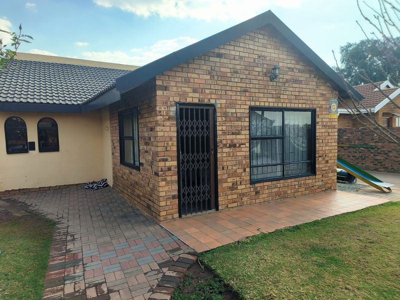 Rear view of the house featuring a face brick facade, tiled patio area, paved walkway, and secure aluminium window frames.