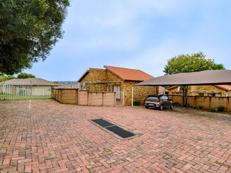 Exterior view of a townhouse featuring a face brick facade, paved driveway, and a shade cloth carport structure.