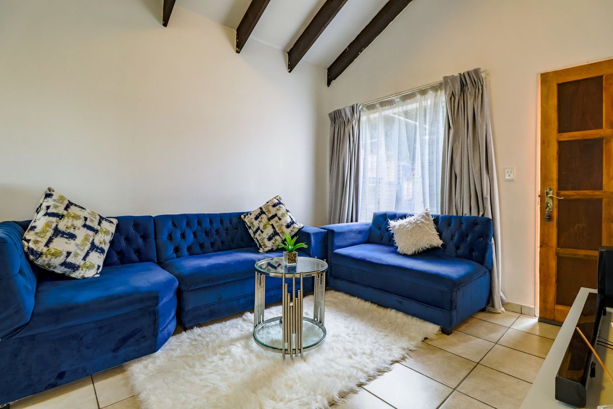 A cozy living room featuring a vaulted ceiling with exposed timber beams, tiled flooring, and a wooden door leading to the exterior.
