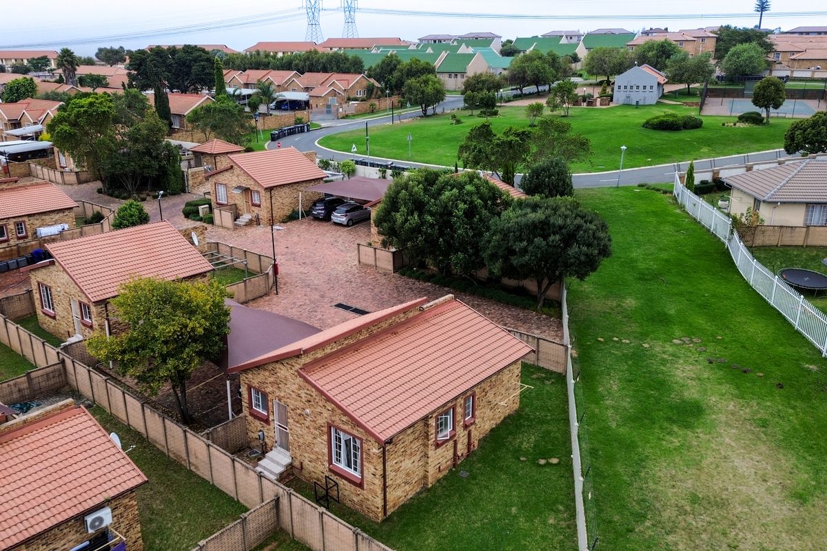 Aerial view of a residential townhouse complex featuring brick-faced units with tiled roofs, paved driveways, carports, and well-maintained communal garden areas.