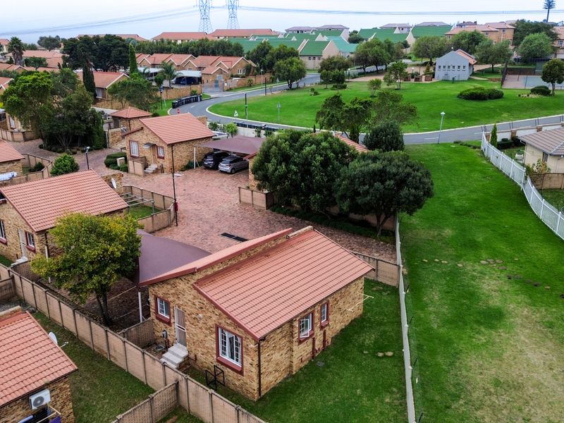 Aerial view of a residential townhouse complex featuring brick-faced units with tiled roofs, paved driveways, carports, and well-maintained communal garden areas.
