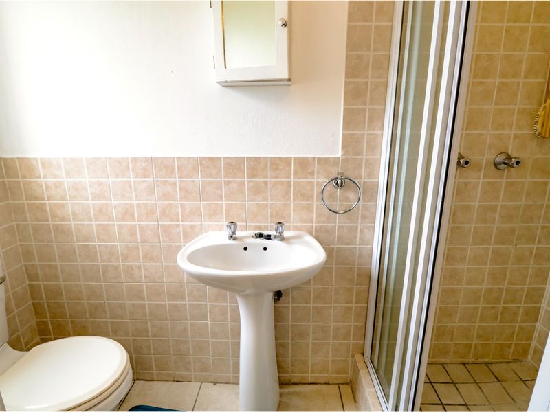 A functional bathroom featuring a pedestal basin, toilet, and a shower enclosure with neutral wall and floor tiling.