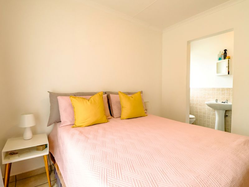 A bedroom featuring a neutral color palette with an adjoining en-suite area containing a pedestal basin and tiled splashback.