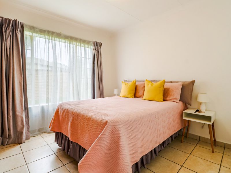 A well-lit bedroom featuring neutral tiled flooring and large windows with installed curtain rails, providing a functional and comfortable living space.