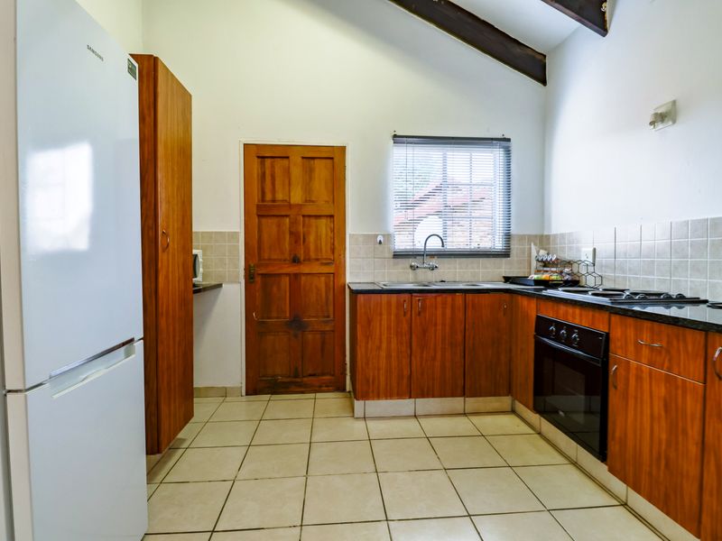 A functional kitchen featuring wooden cabinetry, granite countertops, built-in oven, gas hob, and tiled flooring under an exposed beam ceiling.