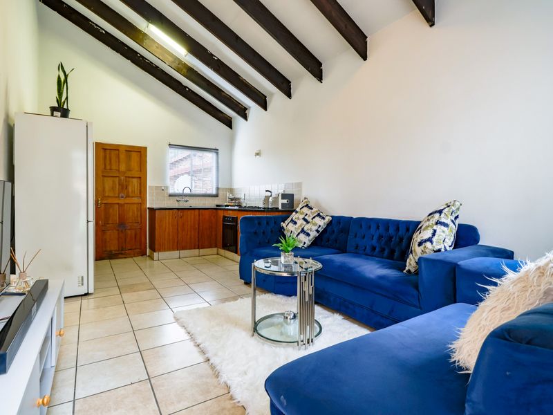 Open-plan living area featuring exposed timber ceiling beams, tiled flooring, and a compact kitchen with built-in cabinetry and oven.
