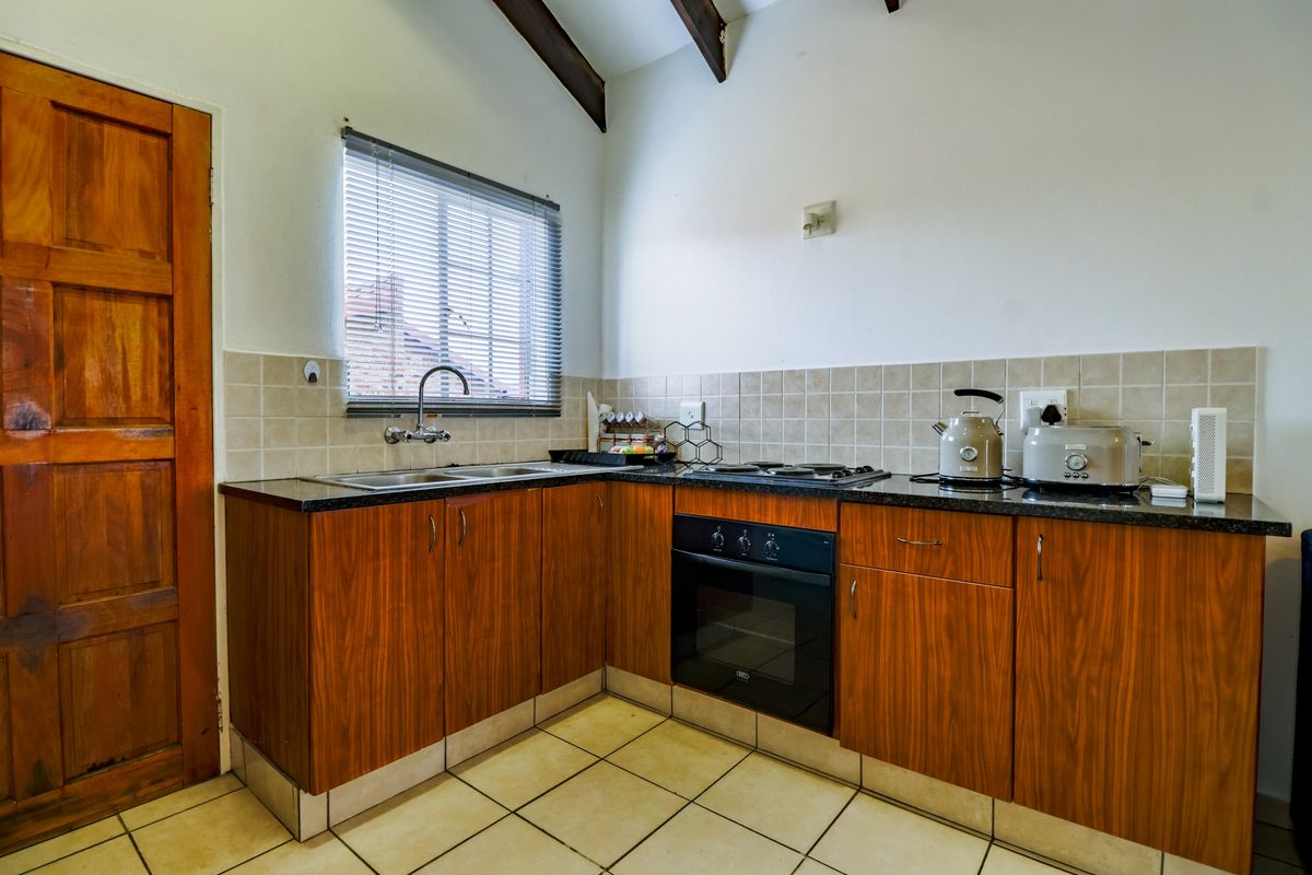 A functional kitchen featuring wood-finish cabinetry, granite countertops, a built-in oven and hob, tiled backsplash, and exposed timber ceiling beams.