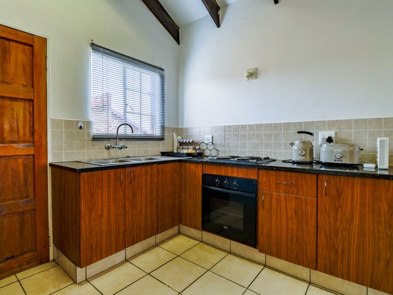 A functional kitchen featuring wood-finish cabinetry, granite countertops, a built-in oven and hob, tiled backsplash, and exposed timber ceiling beams.