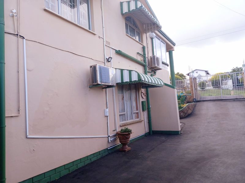 Side view of the property exterior featuring paved driveway, security gate, and wall-mounted air conditioning units with striped window awnings.