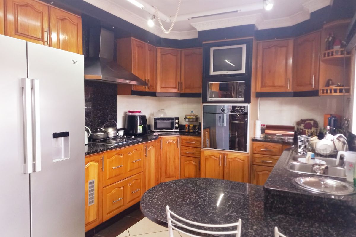 A functional kitchen featuring warm wooden cabinetry, granite countertops, built-in oven, extractor fan, and a breakfast nook area.