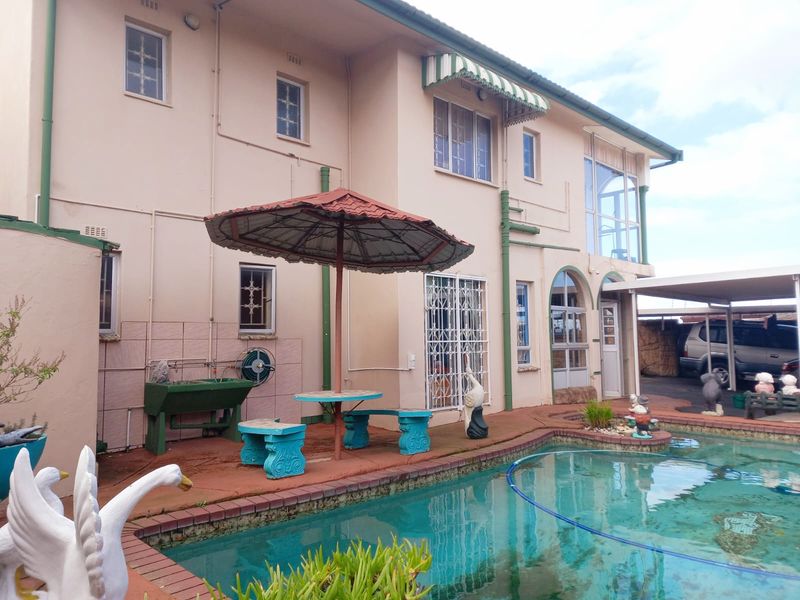 Rear exterior view featuring a swimming pool, paved patio area, and access to the main house structure with security gates and awnings.