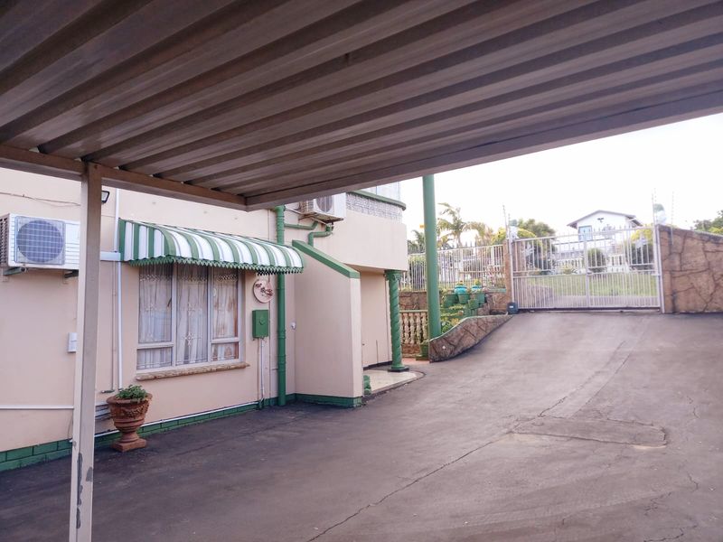 Front exterior view featuring a covered carport, paved driveway, security gate, and an air conditioning unit mounted on the building facade.