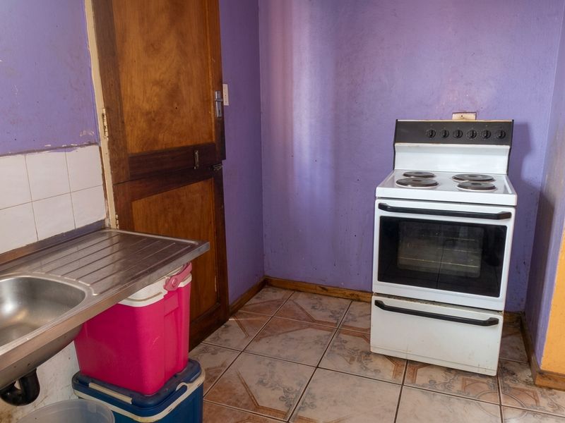 A basic kitchen area featuring a stainless steel sink, tiled flooring, and a freestanding electric stove against purple painted walls.
