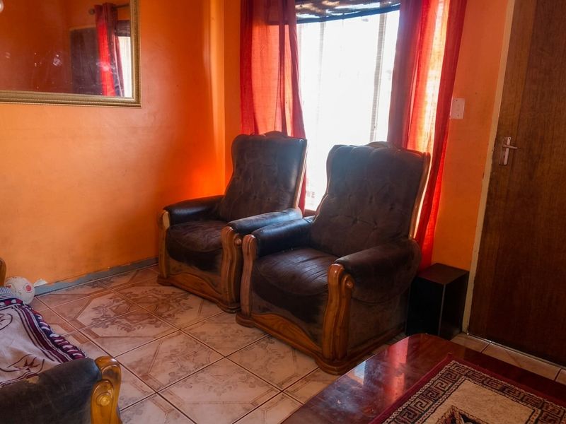 A living room area featuring tiled flooring and a wooden door, providing a functional space for relaxation.