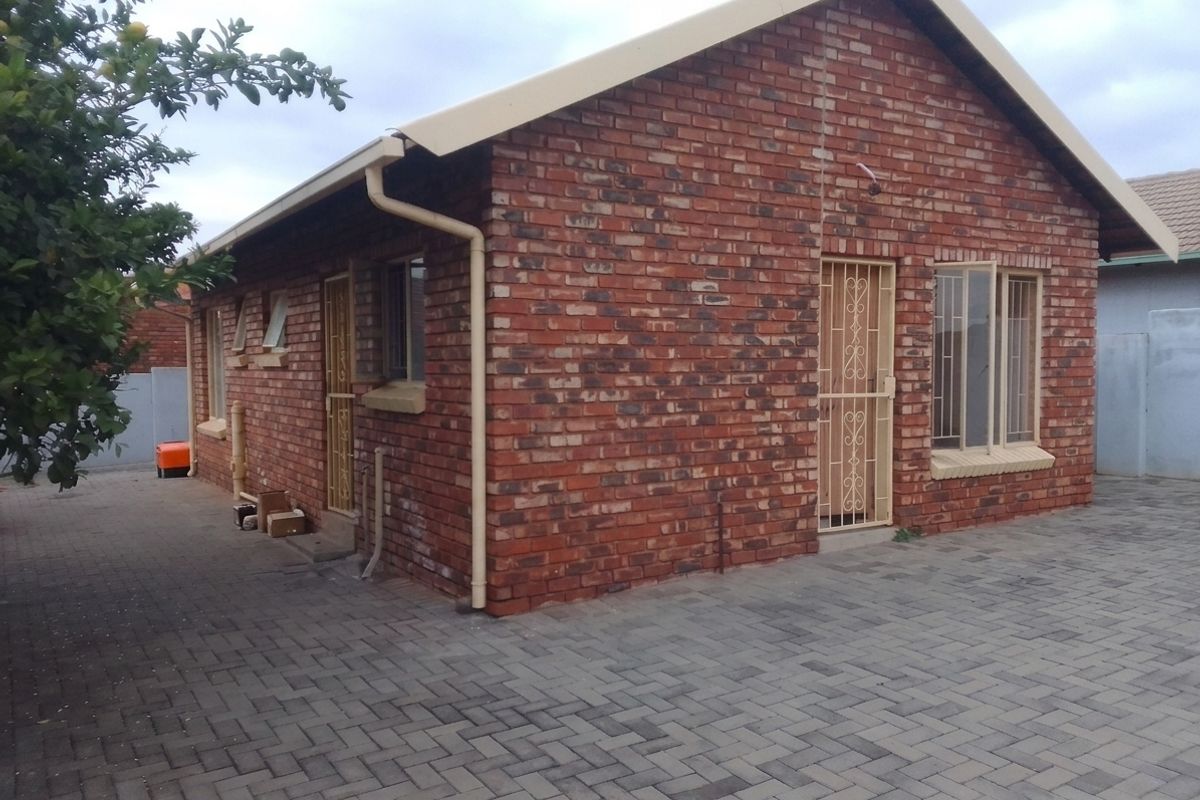 Rear view of a face brick house featuring a paved courtyard, security gates, and functional guttering system.
