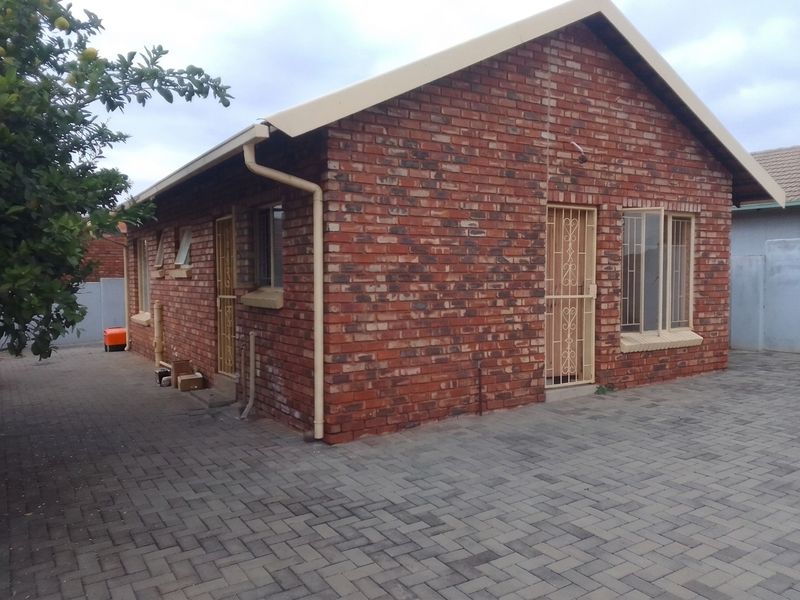 Rear view of a face brick house featuring a paved courtyard, security gates, and functional guttering system.