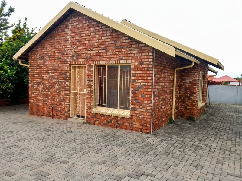 A well-maintained face brick house featuring a paved driveway, secure entrance with metal security gate, and protective window bars.