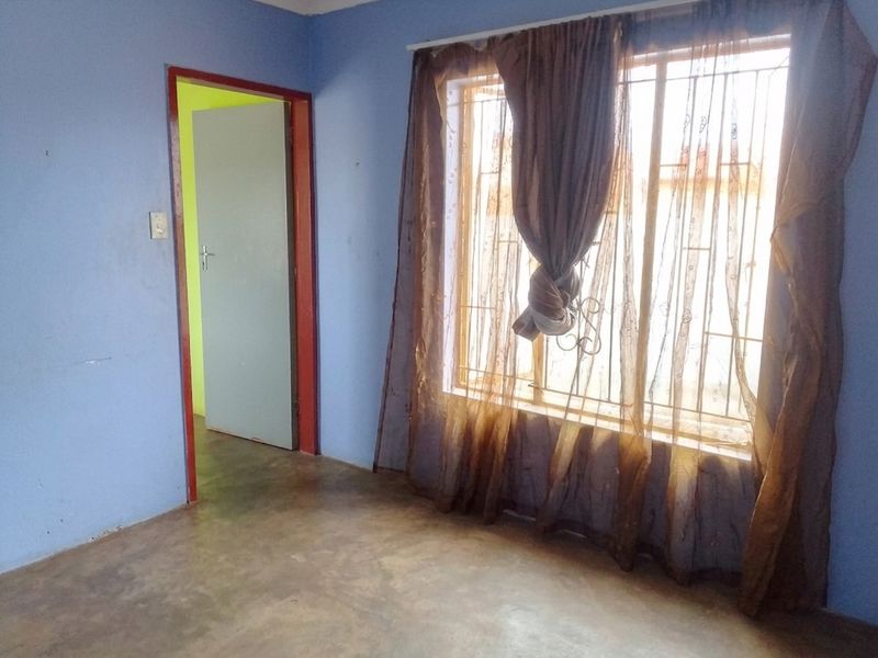 An empty bedroom featuring blue walls, concrete flooring, and a window fitted with security bars.